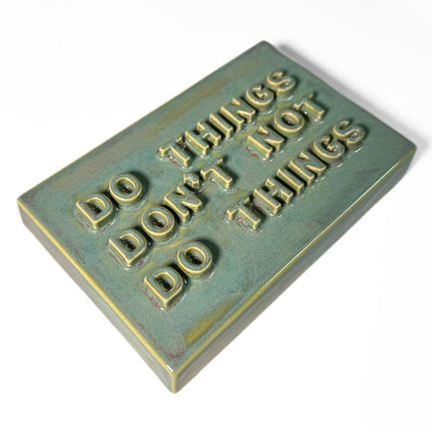 A rectangular ceramic sign with the embossed text 'DO THINGS DON'T NOT DO THINGS' in a teal-green glaze, shown on a plain white background.