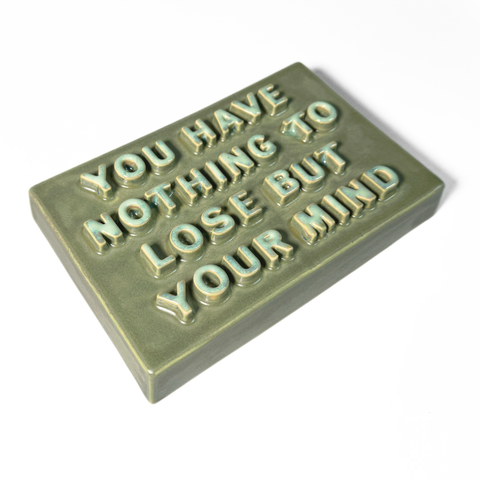 A rectangular ceramic sign with raised lettering that reads 'YOU HAVE NOTHING TO LOSE BUT YOUR MIND' in a light mint green color against a matte sage green background, shown on a plain white background.